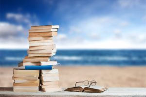 A stack of books and a pair of reading glasses before an empty beach.